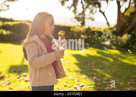 6-year-old girl blowing soap bubbles in garden, with yellow wand and solution bottle, copy space Stock Photo