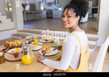 Young woman sitting at round wooden table in home dining area, with breakfast spread, copy space Stock Photo