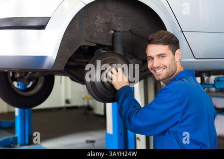 Male mechanic inspecting brake drum under car in repair garage, with blue lift pillars, copy space Stock Photo