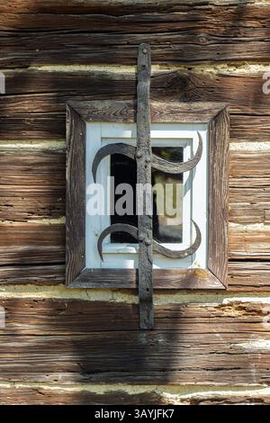 Small window on the wall of an old wooden house with a wrought iron grille. Stock Photo