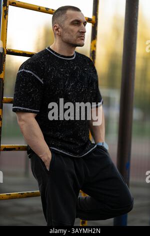 man closely cropped hair stands confidently against yellow playground ladder Stock Photo