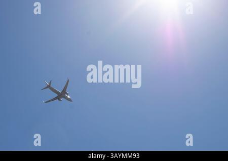 white airplane flying across blue sky Stock Photo
