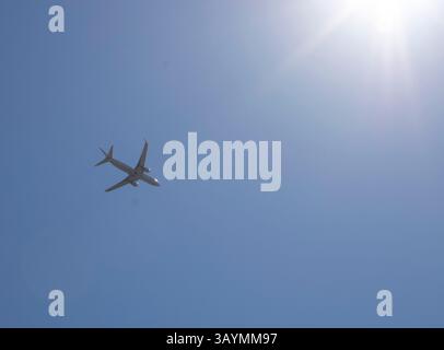 white airplane flying across blue sky Stock Photo