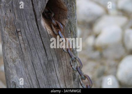 rusted metal chain attached to wood post Stock Photo