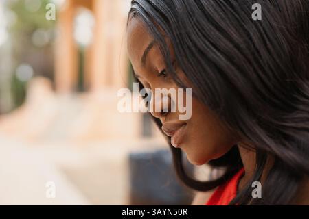 Close-up portrait of a young African American woman with long dark hair. Wearing a red dress. Looking downwards with a serious and thoughtful expressi Stock Photo