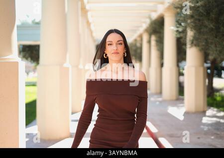 Young stylish woman with long brown hair, wearing a mocha-colored off-the-shoulder dress, Stock Photo