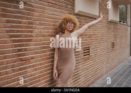 Young woman with afro hair listening music with headphones and making peace sign Stock Photo