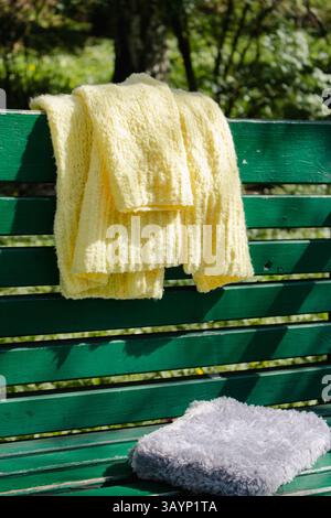Yellow cotton knitted cardigan and grey book cover on green bench. Soft yellow knitted sweater and knitted fluffy book on park bench. Big city fashion Stock Photo