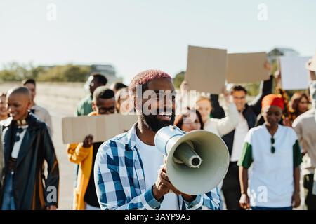 A vibrant group of people participating in a protest, led by a charismatic young man holding a megaphone, expressing a call for unity with signs in ha Stock Photo