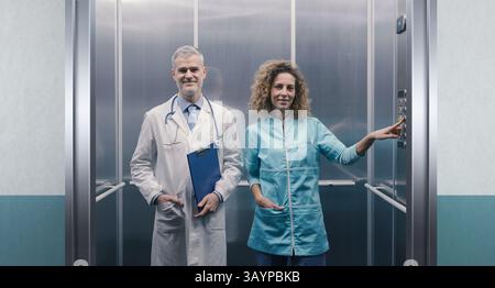 Doctor and nurse standing together in the hospital elevator and smiling Stock Photo