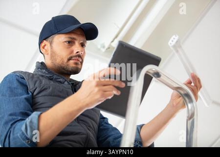 handyman on stepladder holding tablet and new bulb Stock Photo