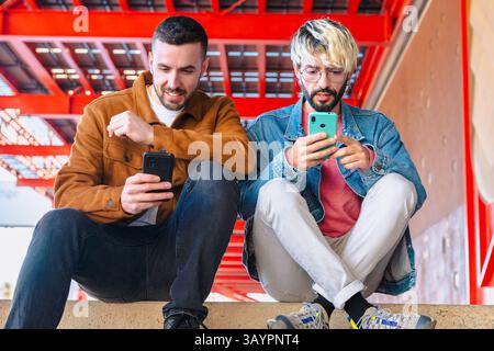 Two Caucasian friends sitting outdoors using smartphones in a modern urban scene Stock Photo