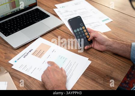 Accountant male uses smartphone app to counts total household bills at corporate workplace Stock Photo