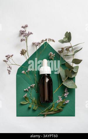 Essential oil in a glass bottle on a green envelope with dried flowers and eucalyptus leaves Stock Photo