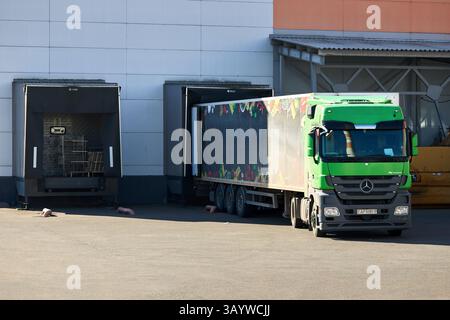 Belarus, Mir - march, 20 2025: Mercedes-Benz Actros 1844 green cabin truck docked near large mall loading dock or loading bay with bumpers, levelers, Stock Photo