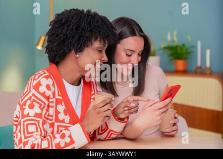 Two happy women sitting on couch smiling while looking at smartphone screen Stock Photo