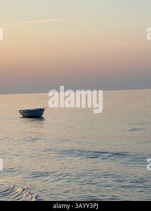Small boat floating gently on the calm Adriatic Sea, surrounded by a vibrant sunset in Pineto, Abruzzo, Italy, creating a serene atmosphere Stock Photo