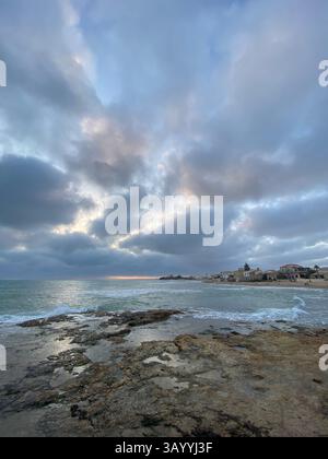 Sunbeams shining through dramatic clouds over a rocky beach in Santa Croce Camerina, Sicily, Italy Stock Photo
