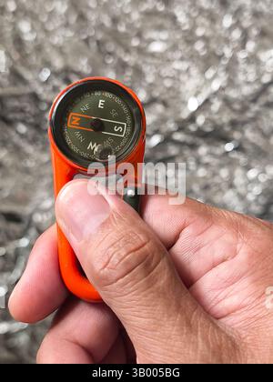 a hanging compass held in the right hand with silver background Stock Photo