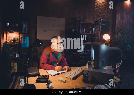 Mature technology specialist working on programming in a cozy home office with vintage decor and professional light for creative tasks. Stock Photo