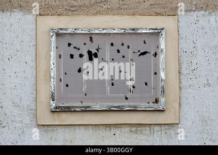 An old, weathered fly screen framed in a rustic wooden frame, mounted on a rough concrete wall. Stock Photo