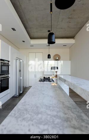Marble countertop island occupying kitchen center, featuring gas cooktop and black pendant lights Stock Photo