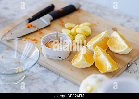 Wooden cutting board showing orange wedges, cubes and juicer with knife on marble counter Stock Photo