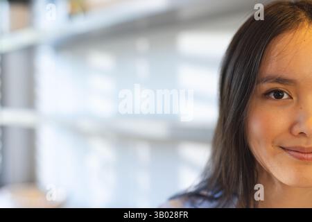 Smiling Asian woman in her twenties looking at camera near window blinds with daylight, copy space Stock Photo