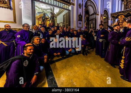 A large group of brotherhood members in purple robes poses for a group photo in the parish church of El Salvador ahead of the Good Friday procession Camino del Calvario. Plaza Salvador, Cuenca, Castilla-La Mancha, Spain. During Semana Santa in Cuenca, 33 Hermandades take part in eleven processions through the city during Holy Week. Stock Photo