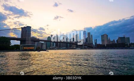 Brooklyn Bridge and Manhattan skyline at sunset. A beautiful sunset view of the Brooklyn Bridge spanning the river with the Manhattan skyline in the Stock Photo
