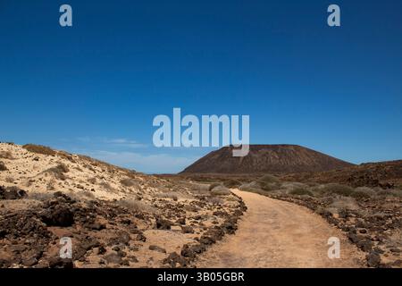A winding dirt path leads through a rugged volcanic terrain toward a flat-topped caldera under a deep blue sky, symbolizing a journey or adventure in Stock Photo