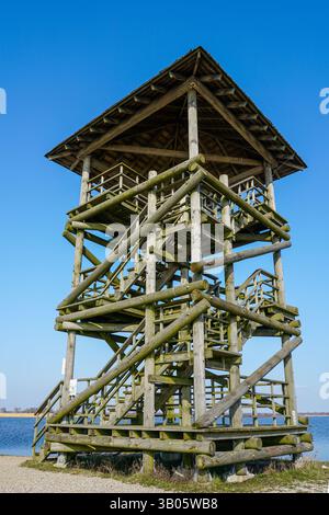 Bird and nature observation tower made of round wooden logs on the edge of a lake, close-up perspective view from bottom to top against the blue sky Stock Photo