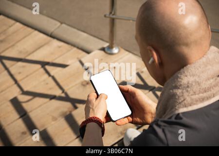 Smartphone in hands sporty man during game interval. Man sitting on stairs using smartphone and texting social media after training. Blank screen. Spo Stock Photo