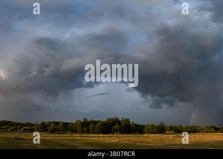 Dark, turbulent storm clouds sweep across the sky while a faint rainbow pierces the edge of the storm Stock Photo