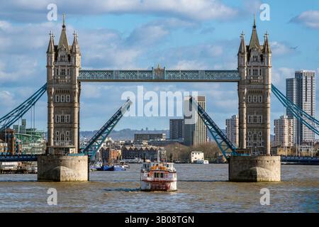 Tower Bridge in London opens to let a boat pass under it, with the city skyline in the background. Stock Photo