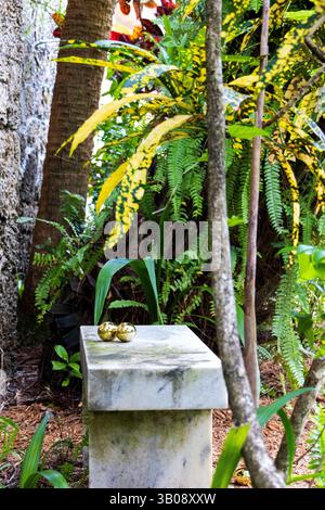 Two golden Easter Eggs nestled together on a stone bench in a cozy nook, set in a tropical garden. Stock Photo