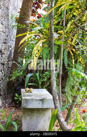 Two golden Easter Eggs nestled together on a stone bench in a cozy nook, set in a tropical garden. Stock Photo