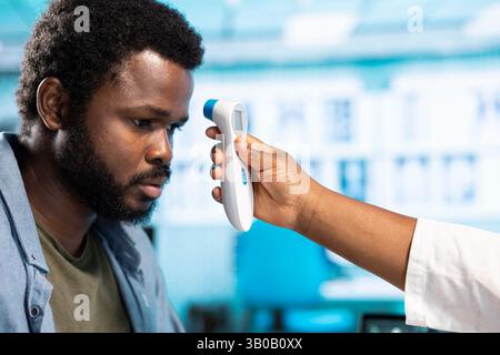 Female doctor measuring the temperature during medical consultation at the cabinet, using a digital thermometer tool to check for flu symptoms. Health expert ensures diagnosis for a patient. Stock Photo
