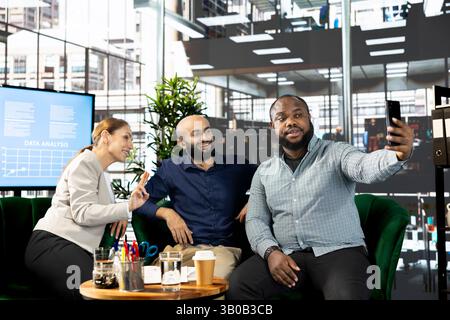 Man and colleagues talking selfie picture after successful briefing meeting to share ideas for profit growth. Employees in office talking photos with smartphone after working on startup evolution vision Stock Photo