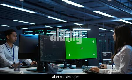 System administrator in data center installing software on green screen computer, troubleshooting issues. IT expert uses mockup PC in server hub, establishing performance benchmarks, camera B Stock Photo