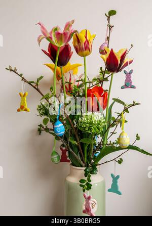 Colorful tulip bouquet in a vase with Easter egg and bunny decorations on branches against a plain backdrop Stock Photo
