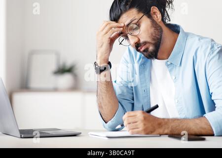 Freelancer Guy Taking Notes To Notepad While Working At Home Office Stock Photo