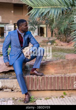 A Stylish Man in a Tailored Suit Poses at an Outdoor Location Surrounded by Nature Stock Photo