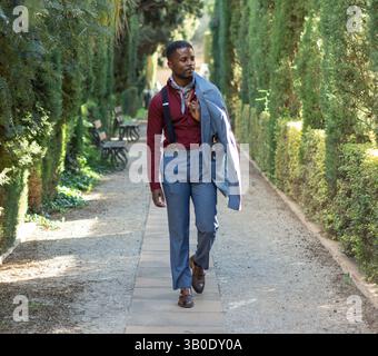 Elegant businessman walking in a formal garden wearing suspenders and carrying jacket Stock Photo
