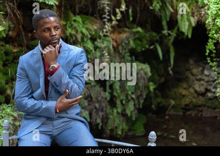 Pensive businessman touching his chin while sitting in a lush garden Stock Photo