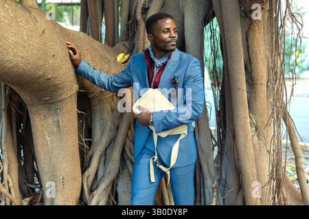 A Stylish Man is Confidently Posing Outdoors in an Elegant Suit Next to a Gorgeous Tree Stock Photo