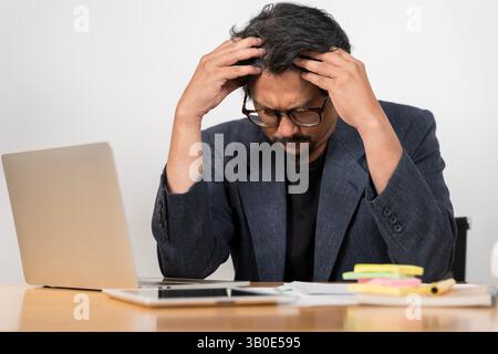 Portrait of a small businessman owner working in front of a laptop having a headache from paying bills or analyzing data. Businessman working on lapto Stock Photo