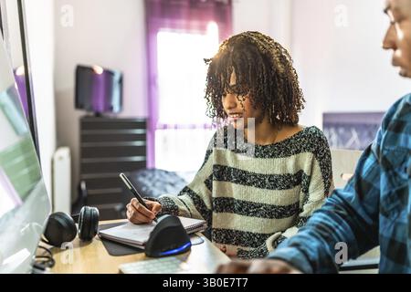 Two programmers working from home, writing notes on notepad while looking at computer screen Stock Photo
