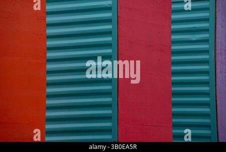 close up of sides of shipping containers painted red green  turquoise purple standing on end showing smooth red side and green corrugated metal side c Stock Photo