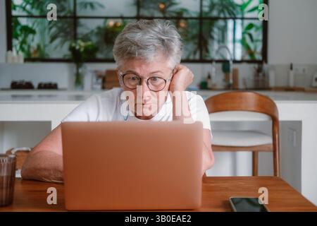 Senior woman with white hair and glasses to improve her vision works on a laptop Stock Photo